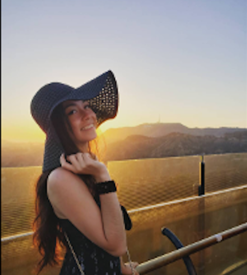 Woman wearing a wide-brimmed hat with a scenic background of mountains and sunset.