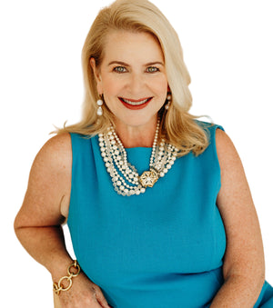woman with red lipstick smiling at camera with a blue shirt and pearls
