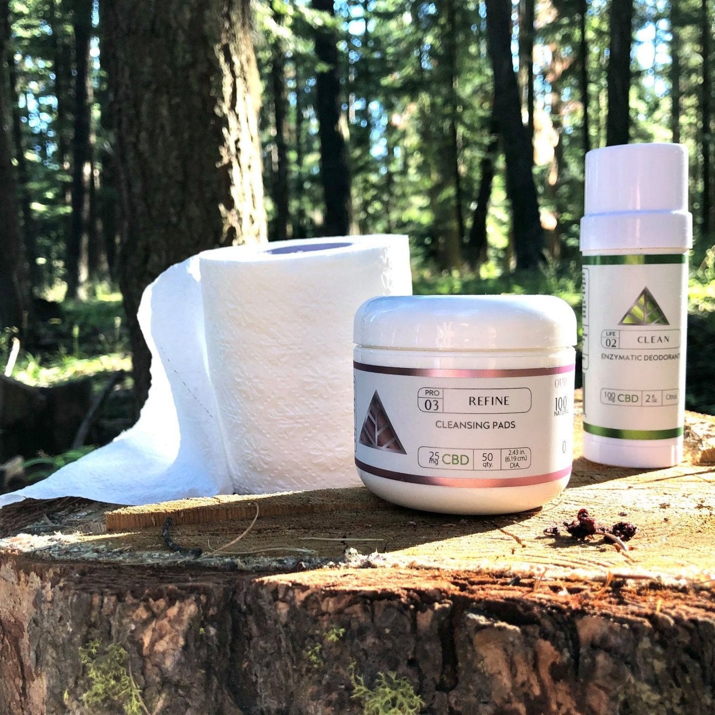 'Color Up Refine Cleansing Pads and Clean Deodorant' on tree stump with trees behind them.