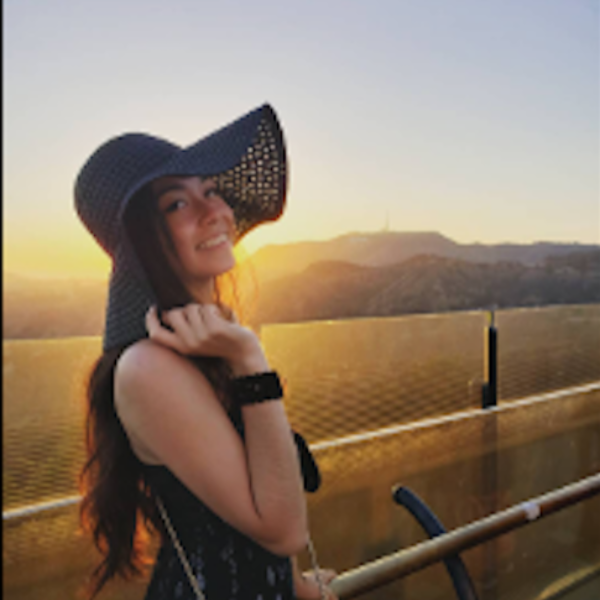 Woman wearing a wide-brimmed hat with a scenic background of mountains and sunset.