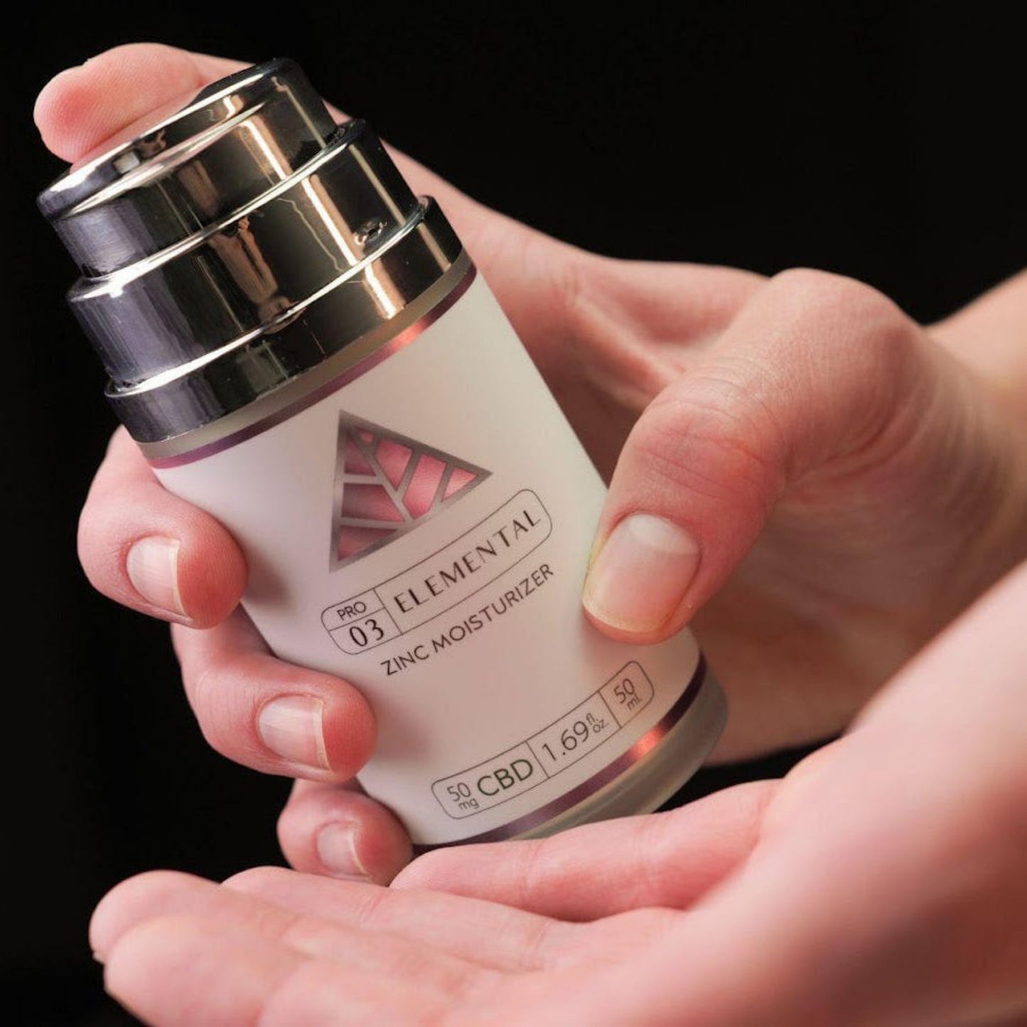 Elemental Zinc Moisturizer with Color Up label in use with two hands holding silver bottle to pump.
