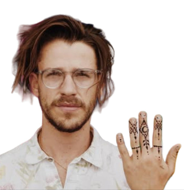 Person with glasses and henna designs on fingers in front of a rainbow flag