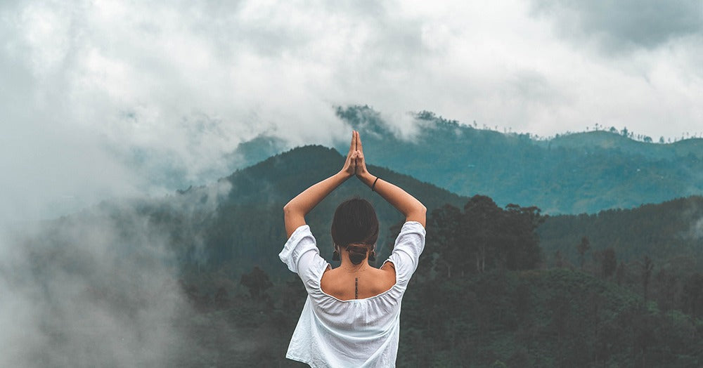 Person in a white shirt practicing yoga with mountains and clouds in the background