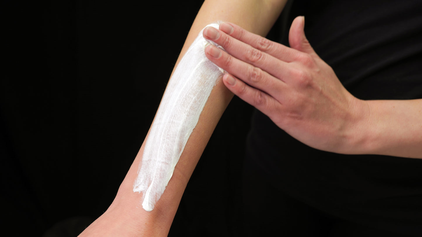 Person applying white 'Color Up' Elemental Zinc Moisturizer cream on their arm against a black background