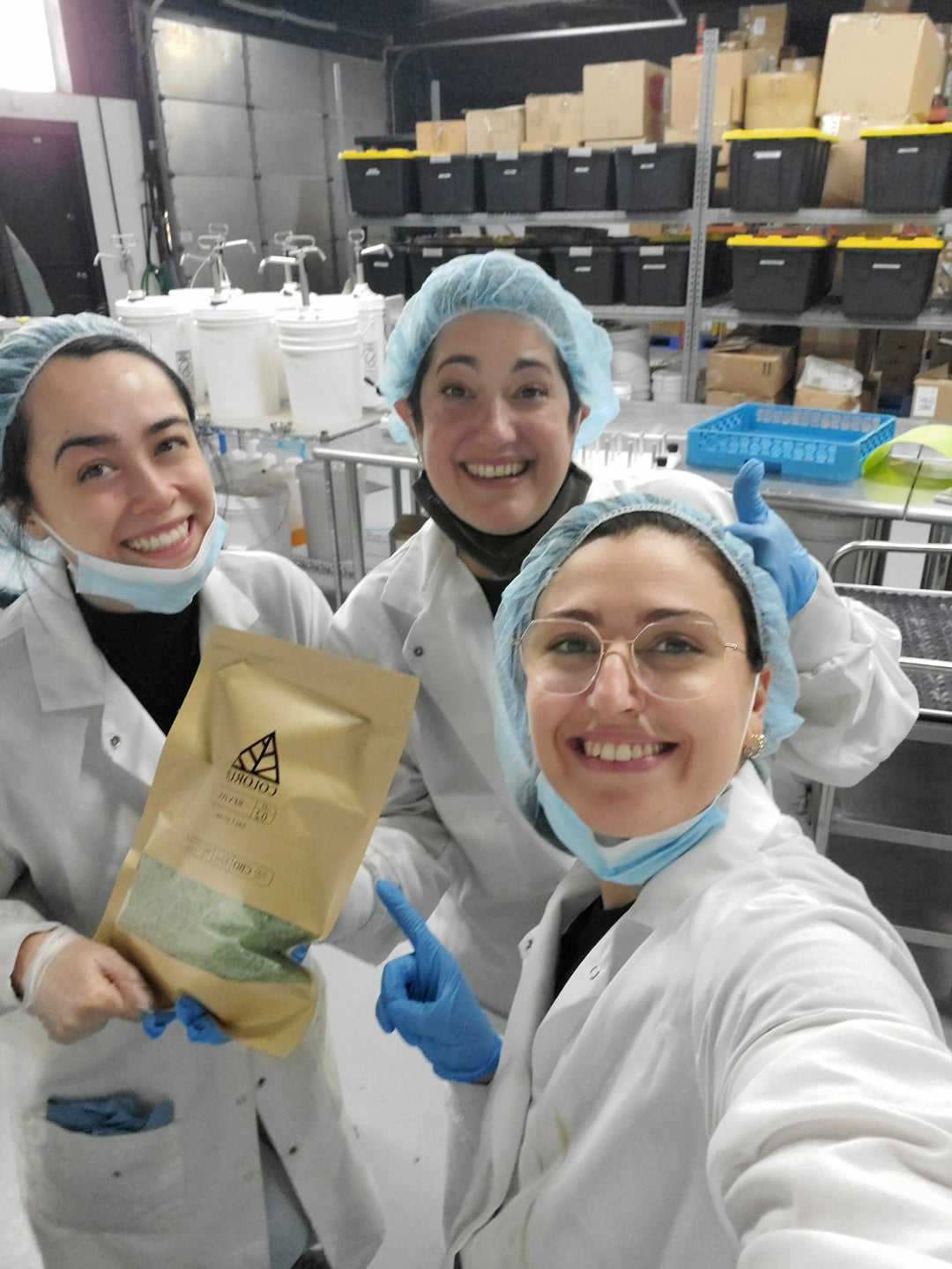 Three women scientists in color up lab smiling at the camera
