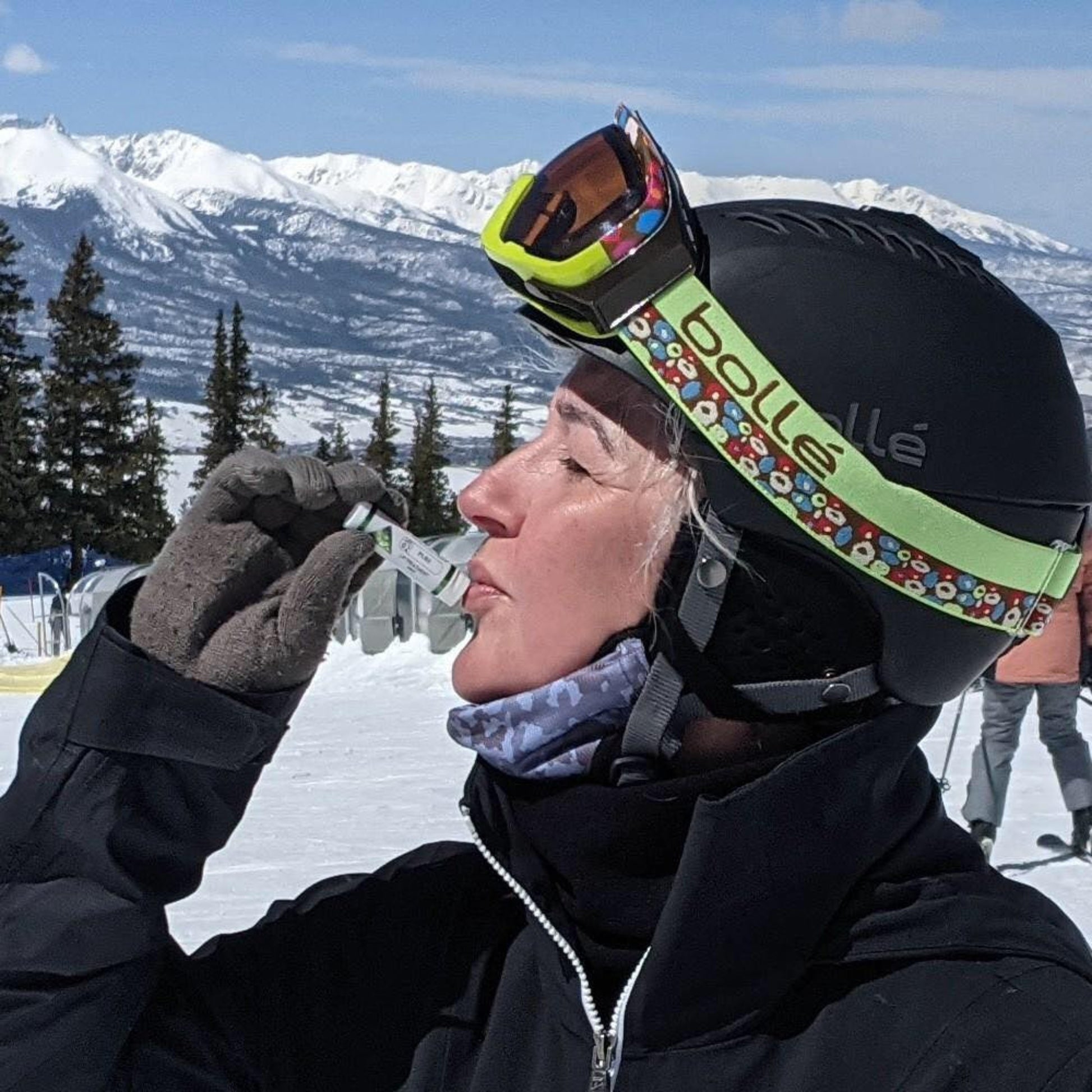 Person in ski gear putting 'Color Up Lip Treatment' on lips with snowy mountains in the background