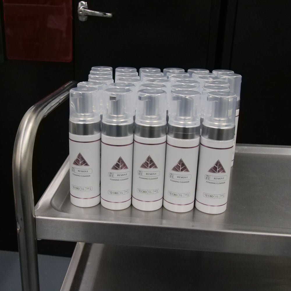 Row of foaming bottles with white label and pink triangle logo over 'Color Up' on a metal shelf in a lab setting.