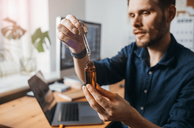 man sitting at desk with a bottle of CBD oil taking CBD every day